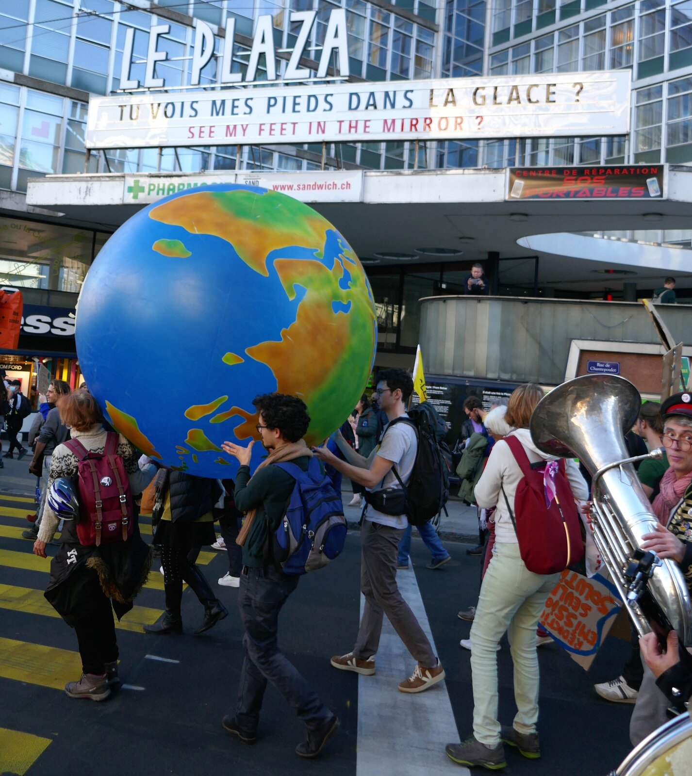Zdjęcie przedstawia uczestników protestu. Na pierwszym planie widoczna jest grupa osób idących ulicą i trzymających duży globus.