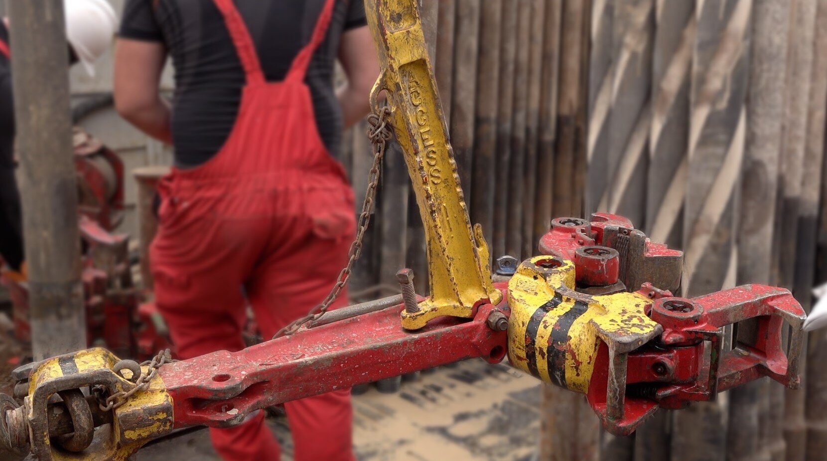 Ilustracja przedstawia masywny, czerwony klucz maszynowy do przewodu wiertniczego. Klucz maszynowy jest w kształcie szczypiec. Klucz podwieszony jest na linie w szybie wiertniczym, z wykorzystaniem przeciwwag. Z jego pomocą stołowi skręcają i rozkręcają połączenia gwintowe przewodu wiertniczego. Klucz maszynowy składa się z: wieszaka klucza maszynowego służącego do podwieszenia klucza na łańcuchu w szybie wiertniczym, szczęki klucza maszynowego która jest elementem zapinanym na zworniku skręcanego elementu rurowego oraz ostrza klucza maszynowego który jest elementem odpowiedzialnym za zwiększenie tarcia między szczękami a zwornikiem skręcanego elementu.