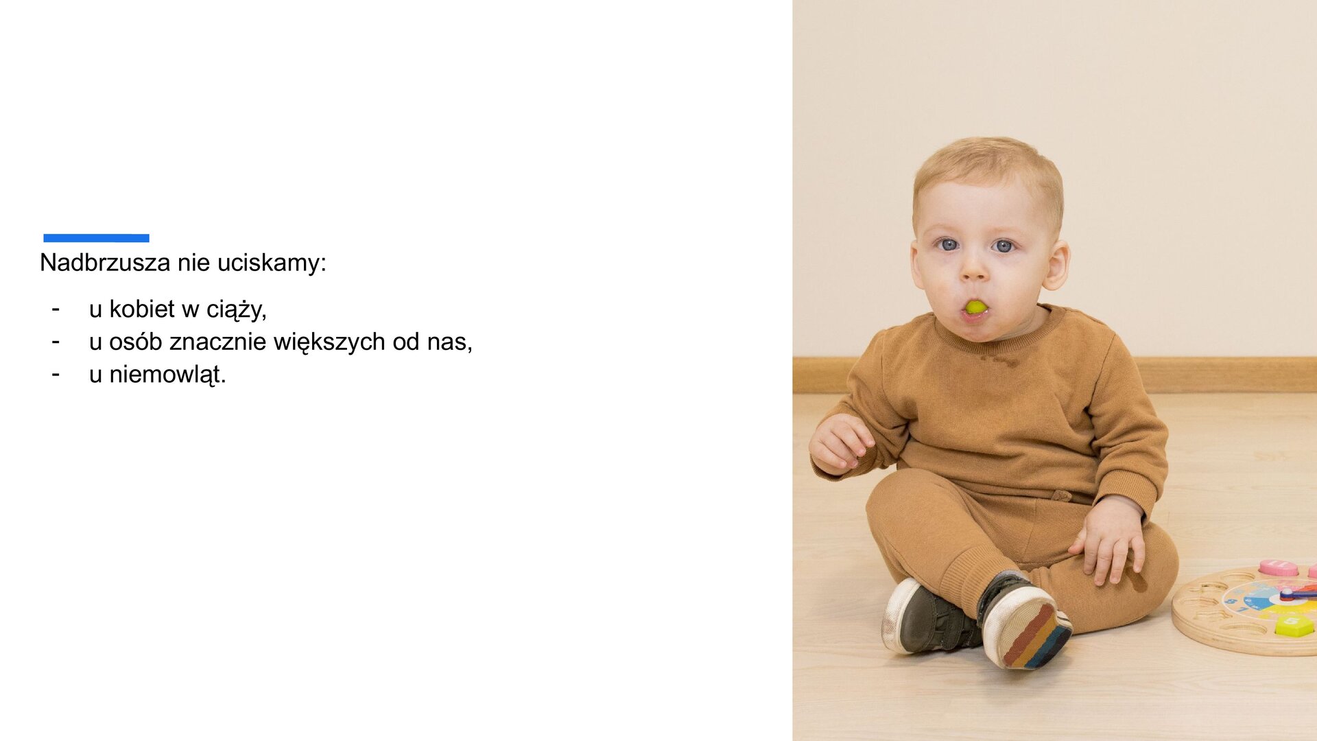 Biały slajd. Z lewej strony tekst: „Nadbrzusza nie uciskamy: u kobiet w ciąży, u osób znacznie większych od nas, u niemowląt”. Z prawej strony zdjęcie przedstawiające małego chłopca w blond włosach i brązowej bluzce oraz spodniach. Chłopiec w trzyma w buzi zielone winogrono.