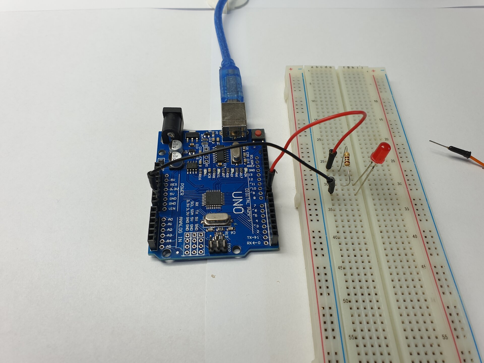 Zdjęcie przedstawia moduł Arduino Uno, podpięty do niego kabel USB oraz diodę LED wpiętą w płytkę stykową. Wolna nóżka rezystora jest podpięta przewodem do pinu D8.