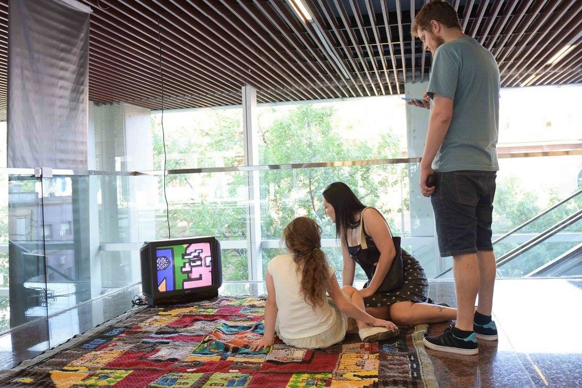Ilustracja przedstawia instalację Tomasza Wlaźlaka pt. „Tkanka”. Składa się ona z dwóch części: animacji komputerowej, wykonanej w 8-bitowej stylistyce wyświetlanej na niewielkim monitorze oraz ręcznie wykonanego dywanu, na którym monitor został umieszczony.