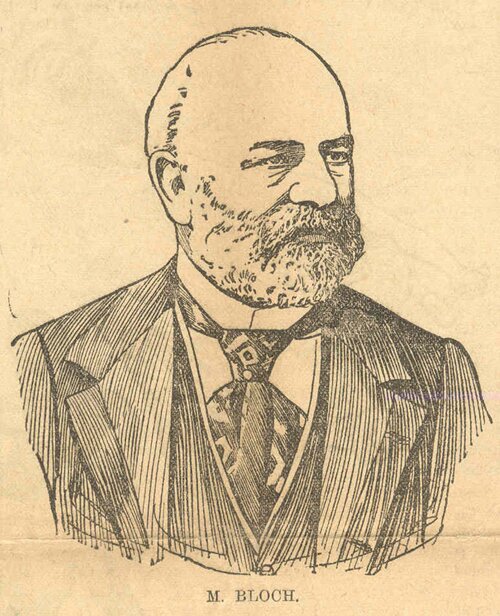 Fotografia przedstawia portret Jana Blocha. To człowiek w średnim wieku, łysiejący i z wąsami oraz brodą, o poważnym wzroku. Ubrany jest w ciemną marynarkę i kamizelkę oraz białą koszulę z usztywnionym kołnierzem i krawat we wzorki.