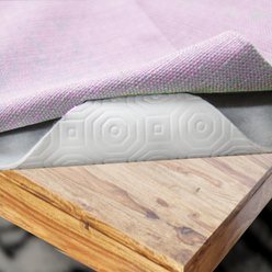 Zdjęcie przedstawia przykładowy podkład z miękkiej tkaniny położony bezpośrednio na drewnianym stole, a na nim fioletowy obrus. Rogi obrusa i podkładu są uniesione odsłaniając kawałek drewnianego blatu stołu.