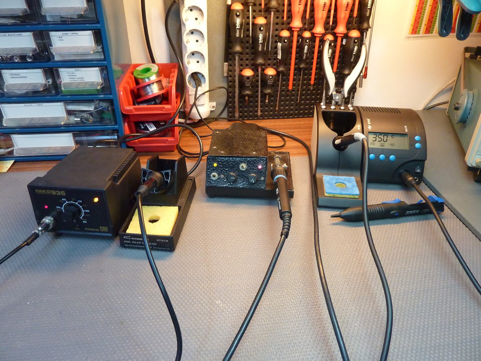 Zdjęcie przedstawia biurko, na którym znajdują się stacje lutownicze, każda w innym rozmiarze, lecz każda z lutownicą grzałkową oraz możliwością zmiany temperatury za pomocą przycisków lub gałki.