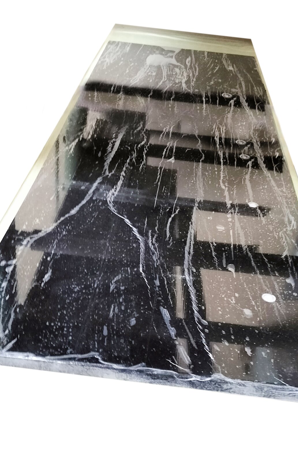 Zdjęcie przedstawia element obudowy pianinowej polakierowany czarnym lakierem poliestrowym, wypolerowany i owinięty folią strecz. Widoczny jest prostokątny element w kolorze szarym z kwadratami i prostokątami w różnym układzie, w kolorze czarnym. Przy lewej i prawej krawędzi oraz na górze widoczny jest jasno szaro‑żółty pas symbolizujący taśmę klejącą.