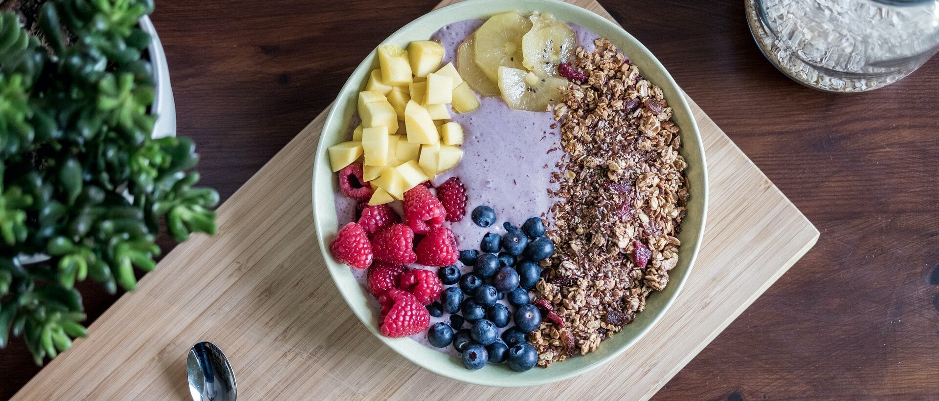 Ilustracja przedstawia miskę z musli, jagodami, malinami i innymi owocami oraz jogurtem.