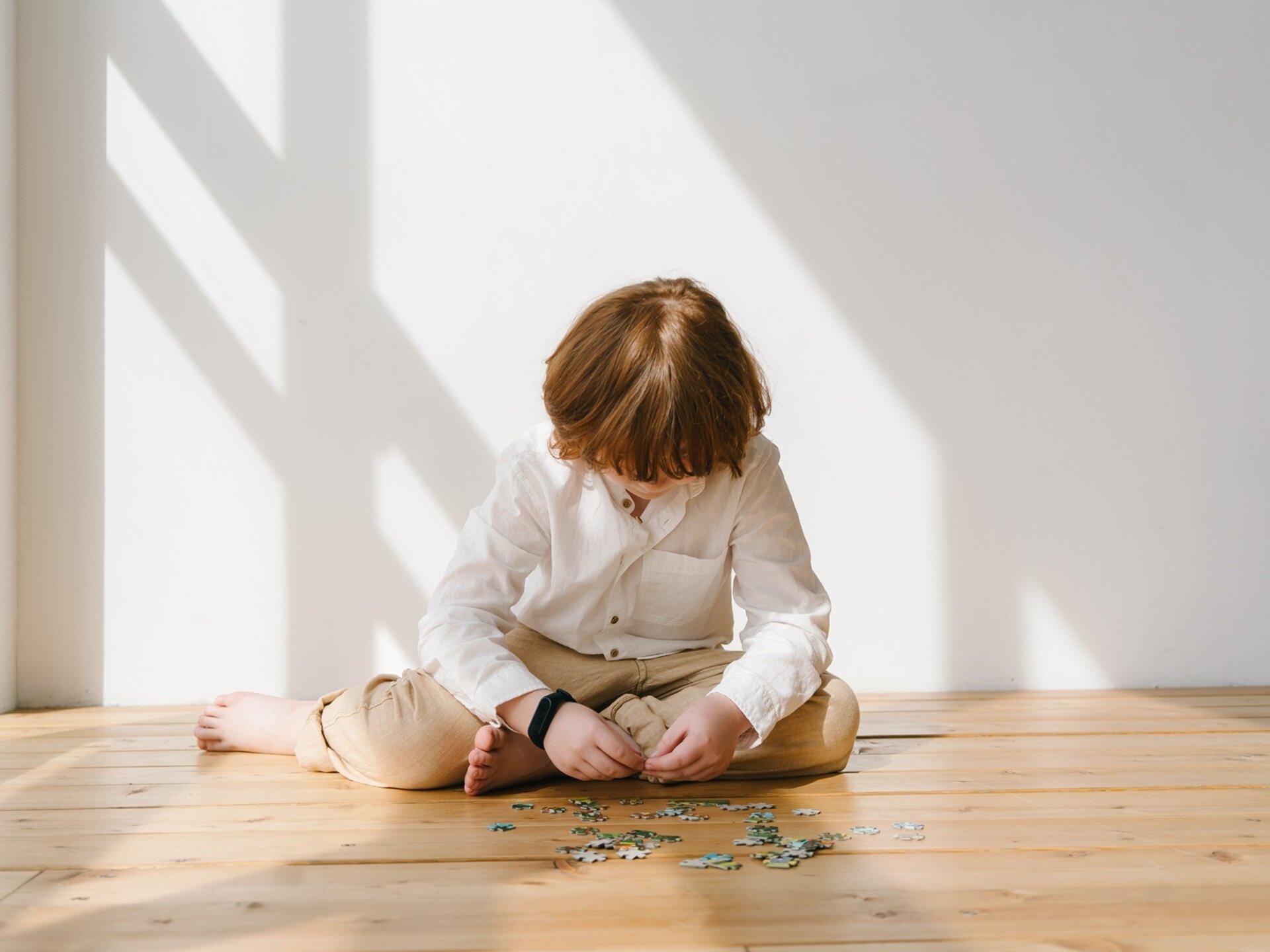 Zdjęcie przedstawia dziecko siedzące na podłodze i układające puzzle.