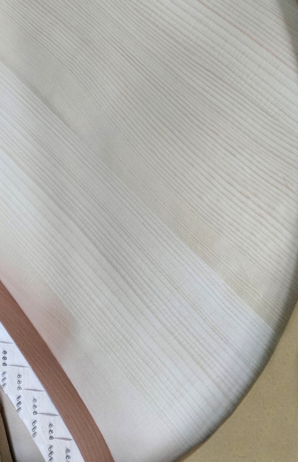 Zdjęcie przedstawia fragment płyty rezonansowej wykonanej z drewna świerkowego. Po prawej stronie widoczny jest fragment półkoliście zakończonej jasnobrązowej płyty. Po lewej stronie widoczny jest biały pas ze srebrnymi kołkami stroikowymi oraz brązowy pas sklejki.