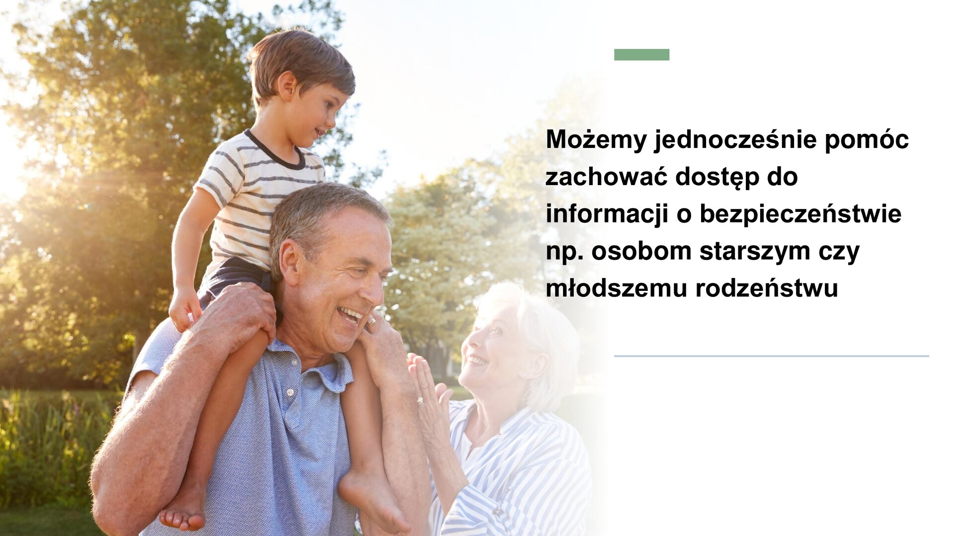 Biały slajd, na którym znajduje się zdjęcie oraz tekst. Z lewej strony slajdu zdjęcie przedstawiające roześmianego starszego mężczyznę. Obok niego stoi roześmiana starsza kobieta. Na barkach mężczyzny siedzi mały chłopiec. W tle zielone krzewy. Z prawej strony tekst: „Możemy jednocześnie pomóc zachować dostęp do informacji o bezpieczeństwie np. osobom starszym czy młodszemu rodzeństwu”.