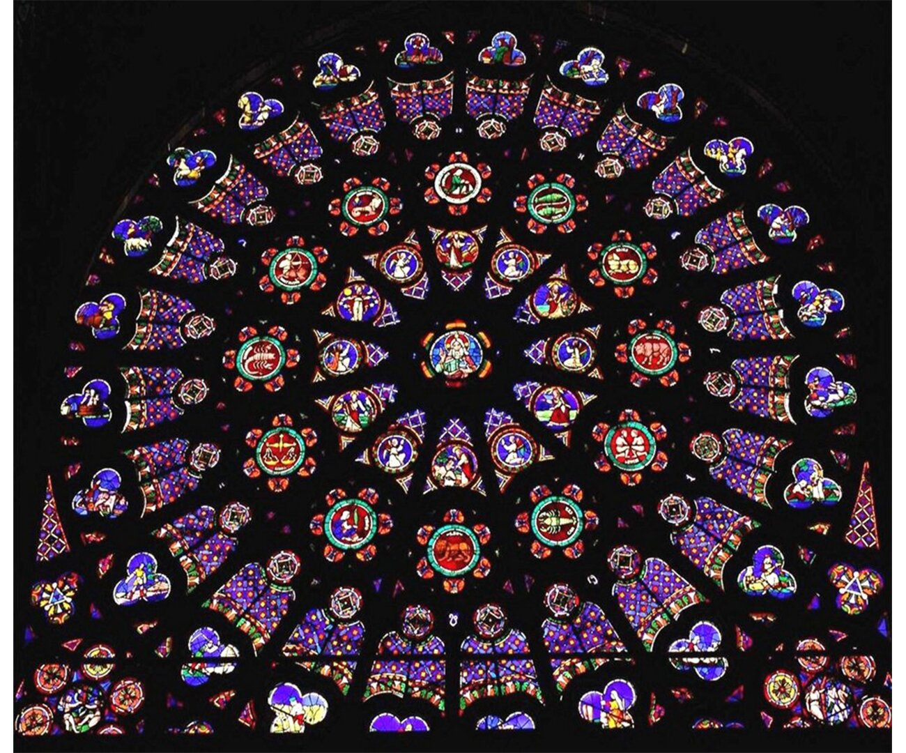 Fotografia barwna przedstawiająca widok na północną rozetę w kościele Saint Denis. Rozeta stworzona z wielu małych, barwnych okienek tworząca jedną całość.