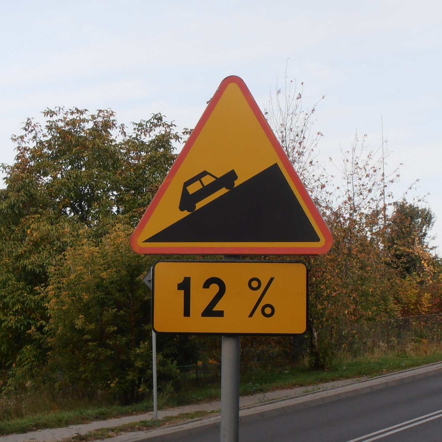 Na zdjęciu widoczny znak ostrzegawczy "stromy podjazd". Pod nim umieszczona jest tabliczka z napisem 12 procent.