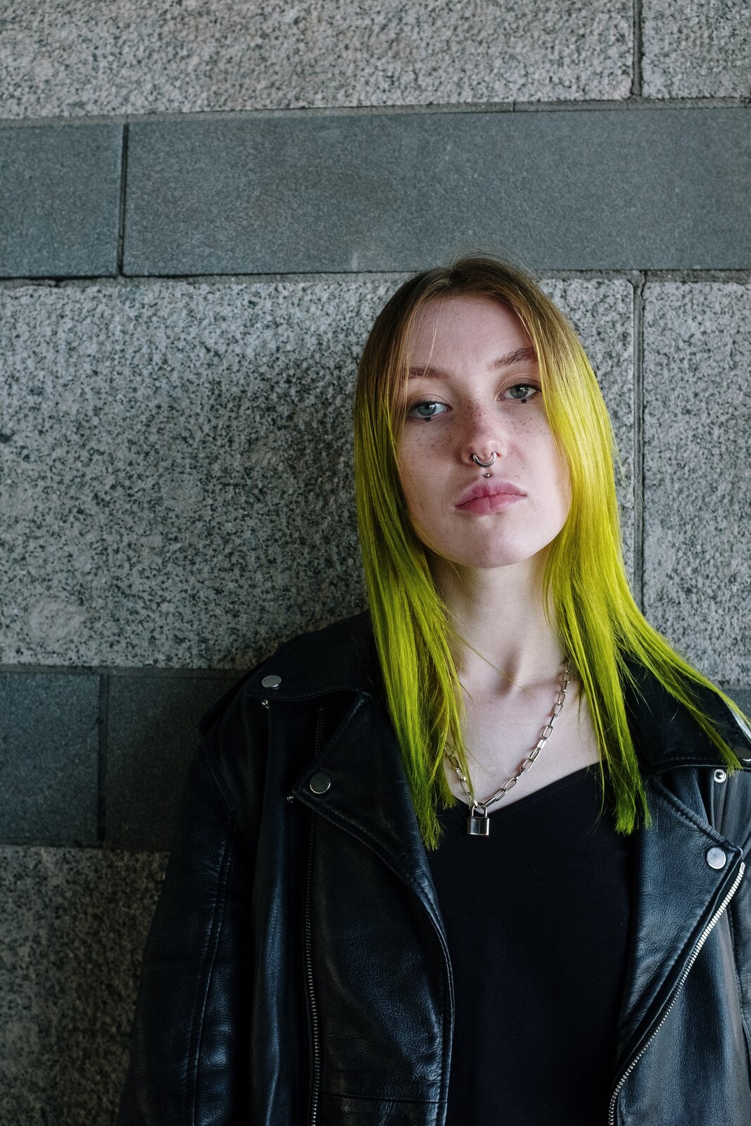 Zdjęcie przedstawia dziewczynę, która ma włosy zafarbowane na zielono. W nosie i nad górną wargą ma kolczyki.