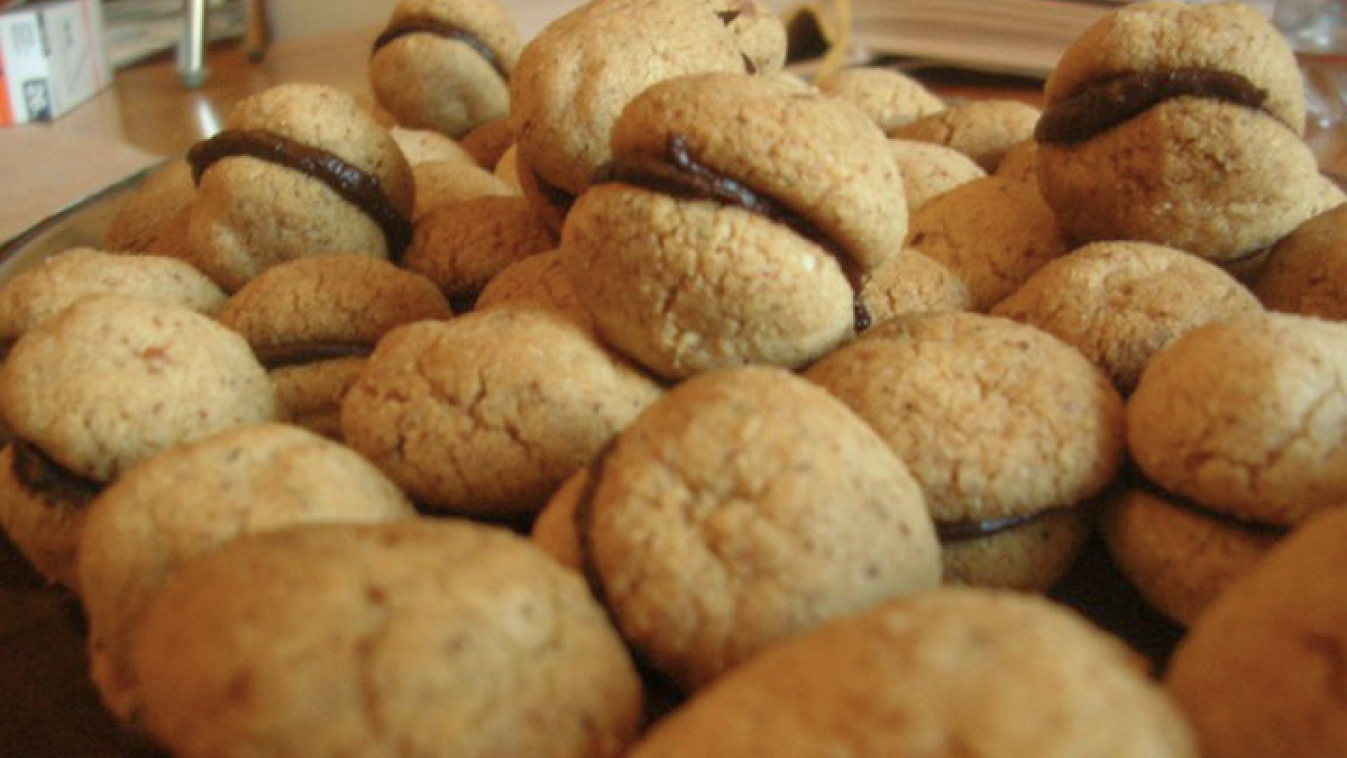 Zdjęcie przedstawia włoskie ciasteczka Baci di dama. Ciasteczka wyglądają jak dwie skorupki połączone czekoladą.