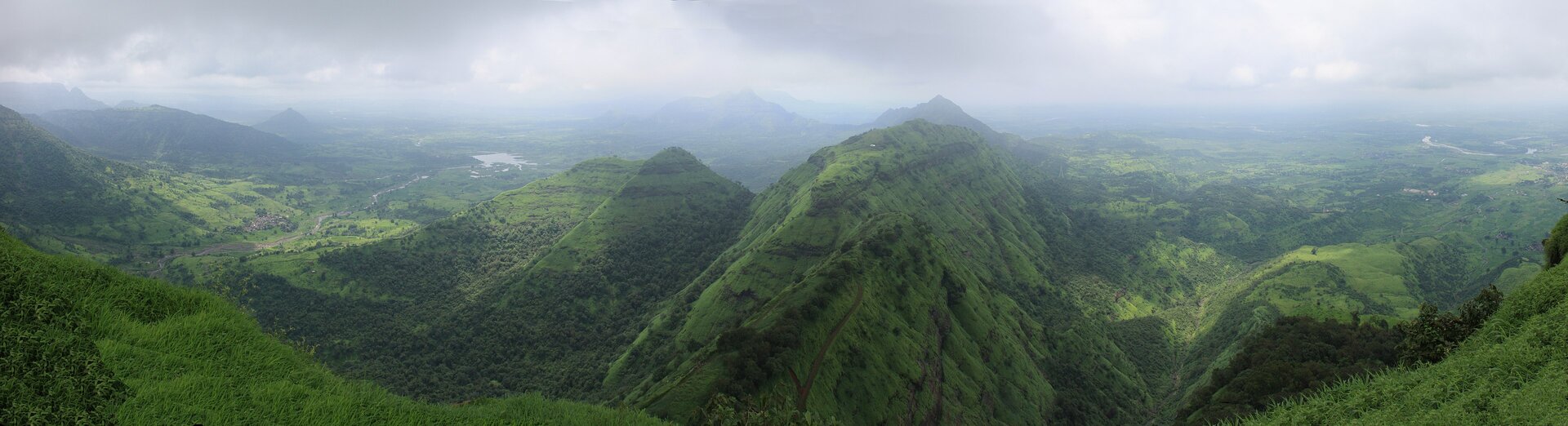 Zdjęcie przedstawia pasmo górskie. Zbocza są zielone, porasta je roślinność. 
