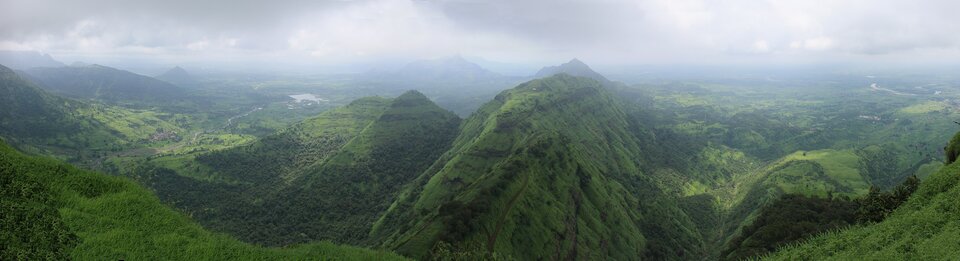 Zdjęcie przedstawia pasmo górskie. Zbocza są zielone, porasta je roślinność. 