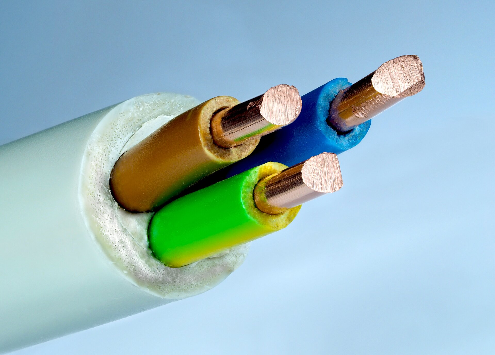 Rys. 4b. Zdjęcie przedstawia kabel trójżyłowy. Składa się on z zewnętrznej, gumowej otoczki w kolorze białym. Wewnątrz otoczki znajdują się trzy przewody miedziane. Jeden otoczony jest gumową izolacją w kolorze brązowym, drugi w kolorze niebieskim, trzeci w kolorze zielono‑żółtym.