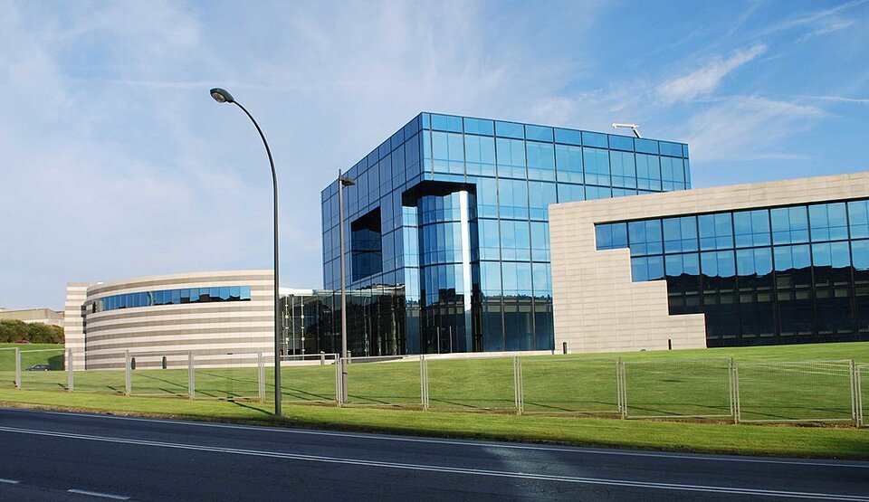 Na fotografii widać siedzibę główną firmy Inditex w Hiszpanii. Składa się ona z trzech części. Część środkowa jest najwyższa. Jest to oszklony, wysoki gmach w kształcie prostokąta. Jedna z bocznych części budynku ma białe ściany i duże okna, z kolei druga ma bardziej zaokrągloną bryłę i mniejsze okna od poprzedniej.