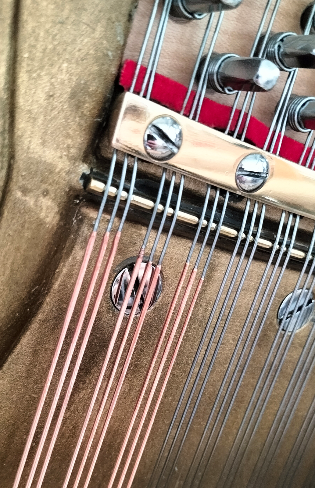 Zdjęcie przedstawia struny stalowe i miedziane zamontowane w pianinie. Widoczne są trzy wiązki strun miedzianych oraz pięć wiązek strun staowych.