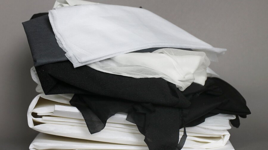 Na zdjęciu znajdują się złożone, ułożone jeden na drugim materiału w kolorach białym oraz czarnym.