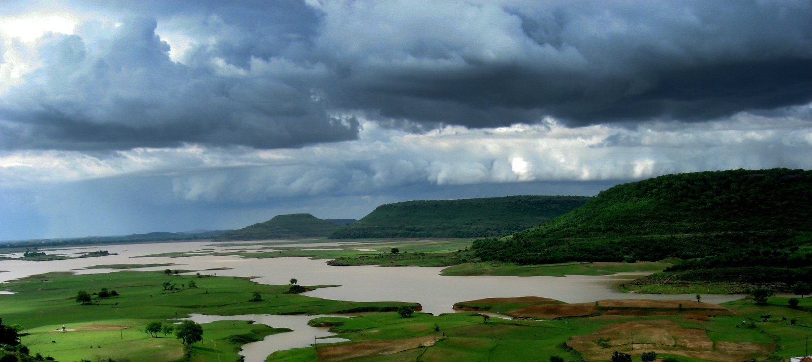 Zdjęcie przedstawia krajobraz uchwycony podczas pory monsunowej w Indiach. Porę tę charakteryzuje duże zachmurzenie i ogromne sumy opadów. Na fotografii znajdują się niewielkie, płasko zakończone wzgórza porośnięte zieloną roślinnością. U ich podnóża widoczne są zielone tereny porośnięte gdzieniegdzie drzewami. Płaskowyż jest w większości zalany wodą. Niebo na zdjęciu jest ciemne, są na nim gęste, skłębione chmury.