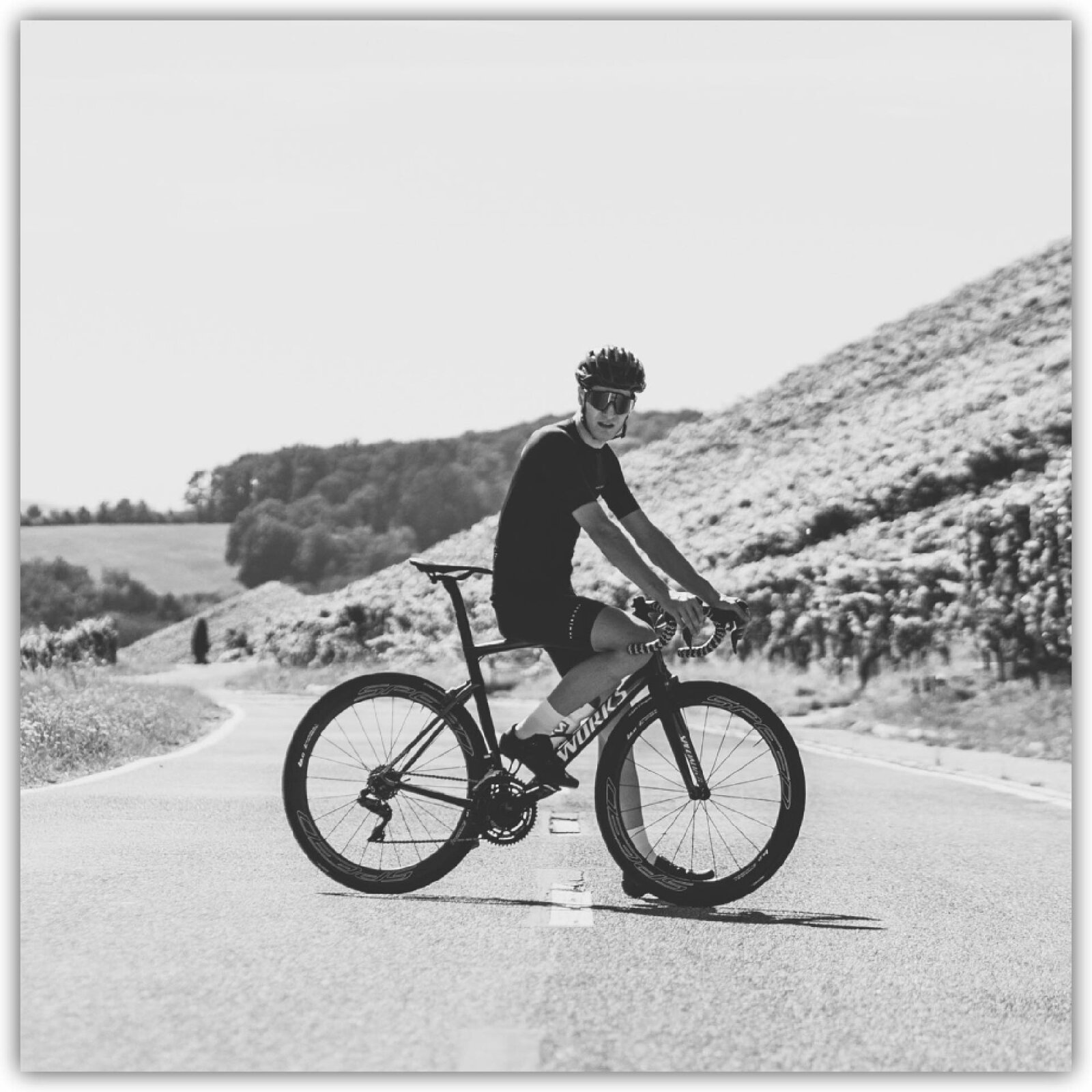 Ilustracja przedstawia mężczyznę na rowerze w kasku na szosie. W tle przyrodniczy krajobraz.