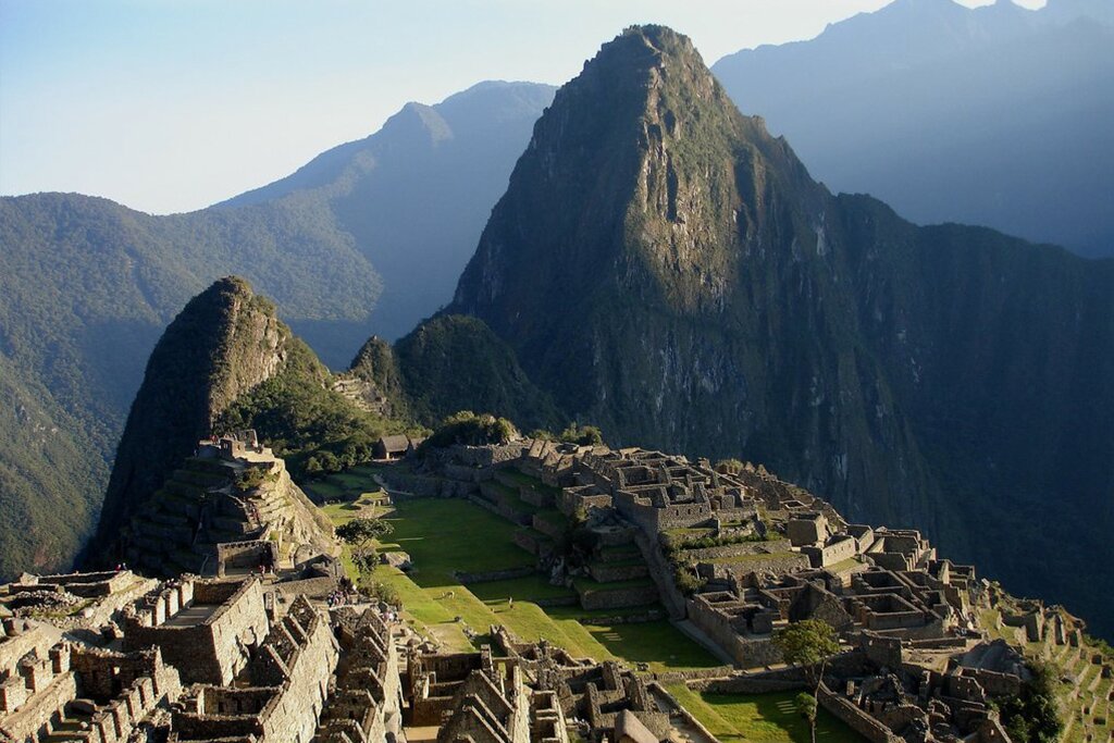 Fotografia przedstawiająca Machu Picchu – najlepiej zachowane miasto Inków. Góry porośnięte zieloną roślinnością. U ich stóp kamienne miasto.