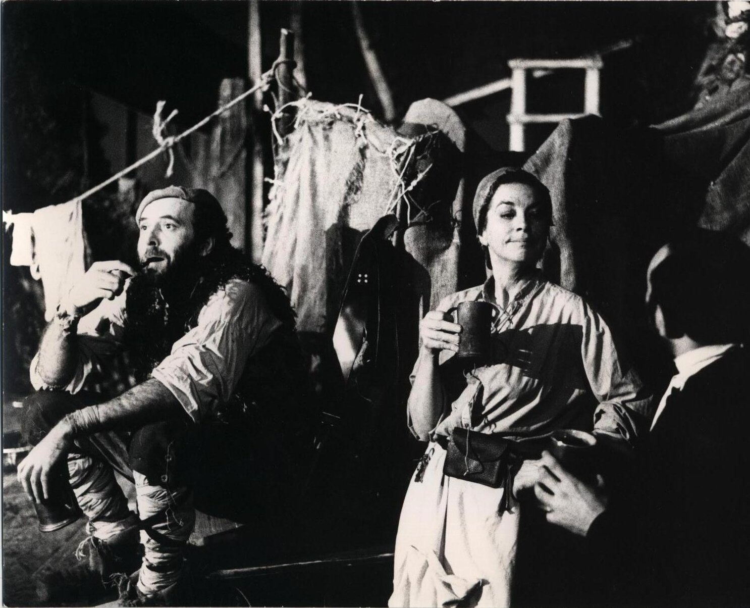 Ilustracja przedstawia aktorów: kobietę i mężczyznę ubranych w stroje chłopskie, którzy instruowani są przez mężczyznę w garniturze (reżysera). Kobieta ubrana jest w koszulę zapinaną na guziki, spódnicę, na głowie ma chustkę, zasłaniającą włosy. Przy pasie niewielka, skórzana torebka. W ręku trzyma kubek. Obok niej siedzi mężczyzna ubrany w białą koszulę z podwiniętymi rękawami. Na nogach ma spodnie, których nogawki owinięte są w onuce. W lewym ręku trzyma metalowy kubek, w prawym fajkę. Na koszuli ma kamizelę z owczego futra, na głowie nakrycie głowy przypominające beret. Za nimi rozciągają się sznurki na bieliznę, drewniana konstrukcja, na której wisi kawałek materiału, płótna. Mężczyzna w garniturze stoi do widza tyłem, twarzą do kobiety, z którą rozmawia. 