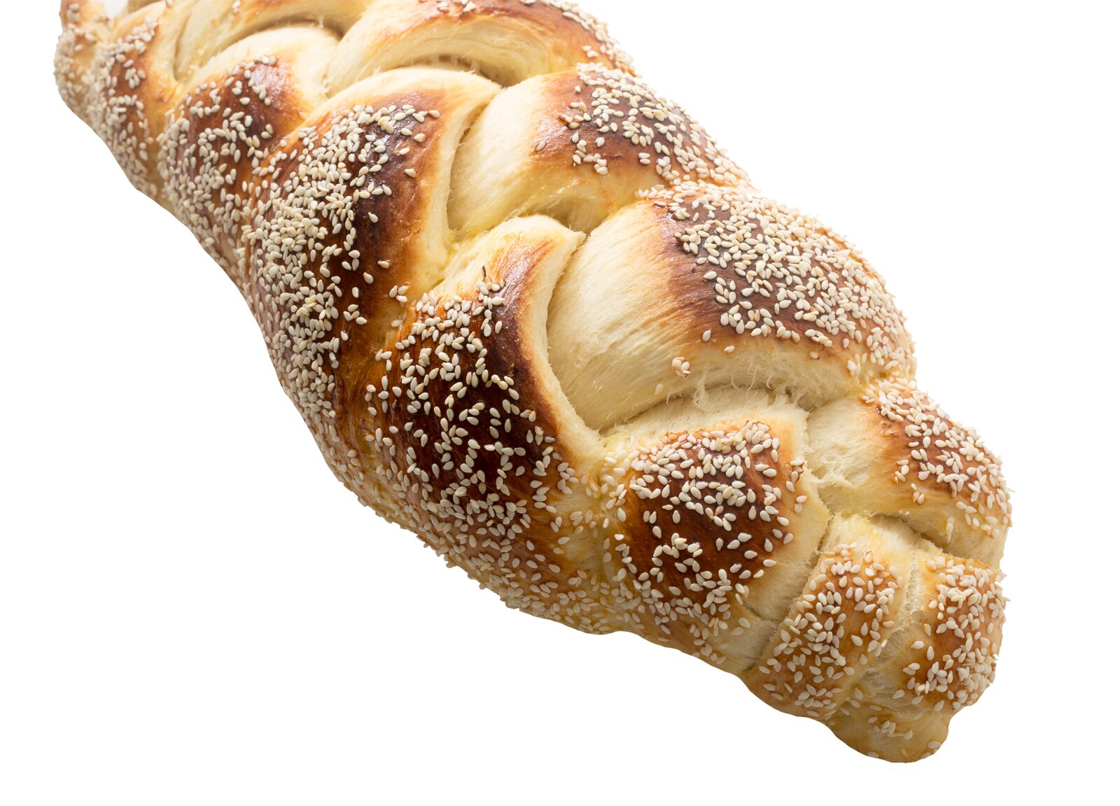 Zdjęcie przedstawia fragment chałki na białym tle. Ujęcie wyjęcie jest od góry pod kątem. Chałka ma kształt podłużny, owalny z widocznymi uwypukleniami przeplatających się warkoczy ciasta. Wierzch bułki jest w kolorze od jasnobrązowego do ciemnozłocistego oraz obsypany jest białym sezamem.