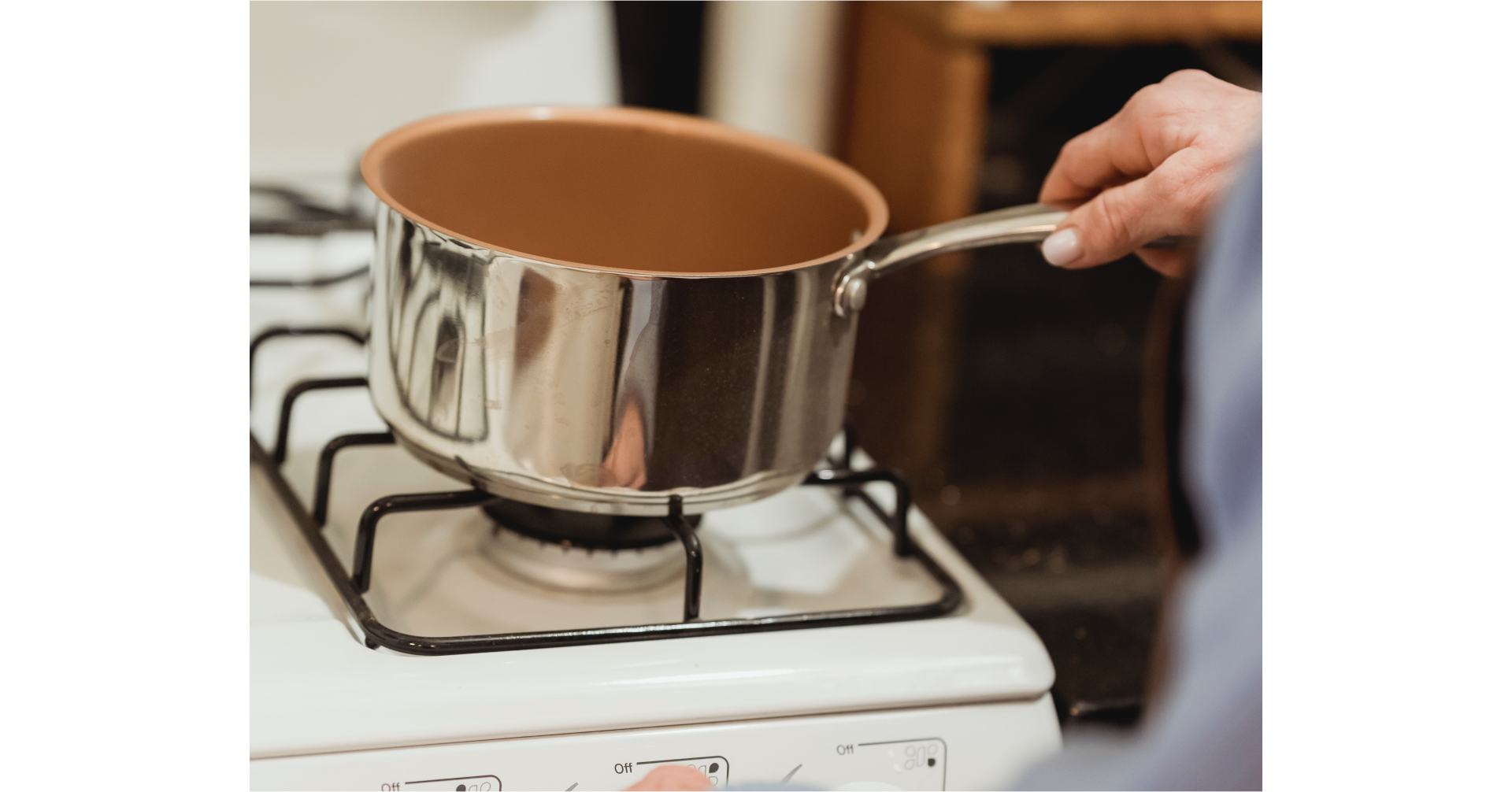 Kuchenka gazowa z umieszczonym na ruszcie rondelkiem i ręka trzymająca go za rączkę.