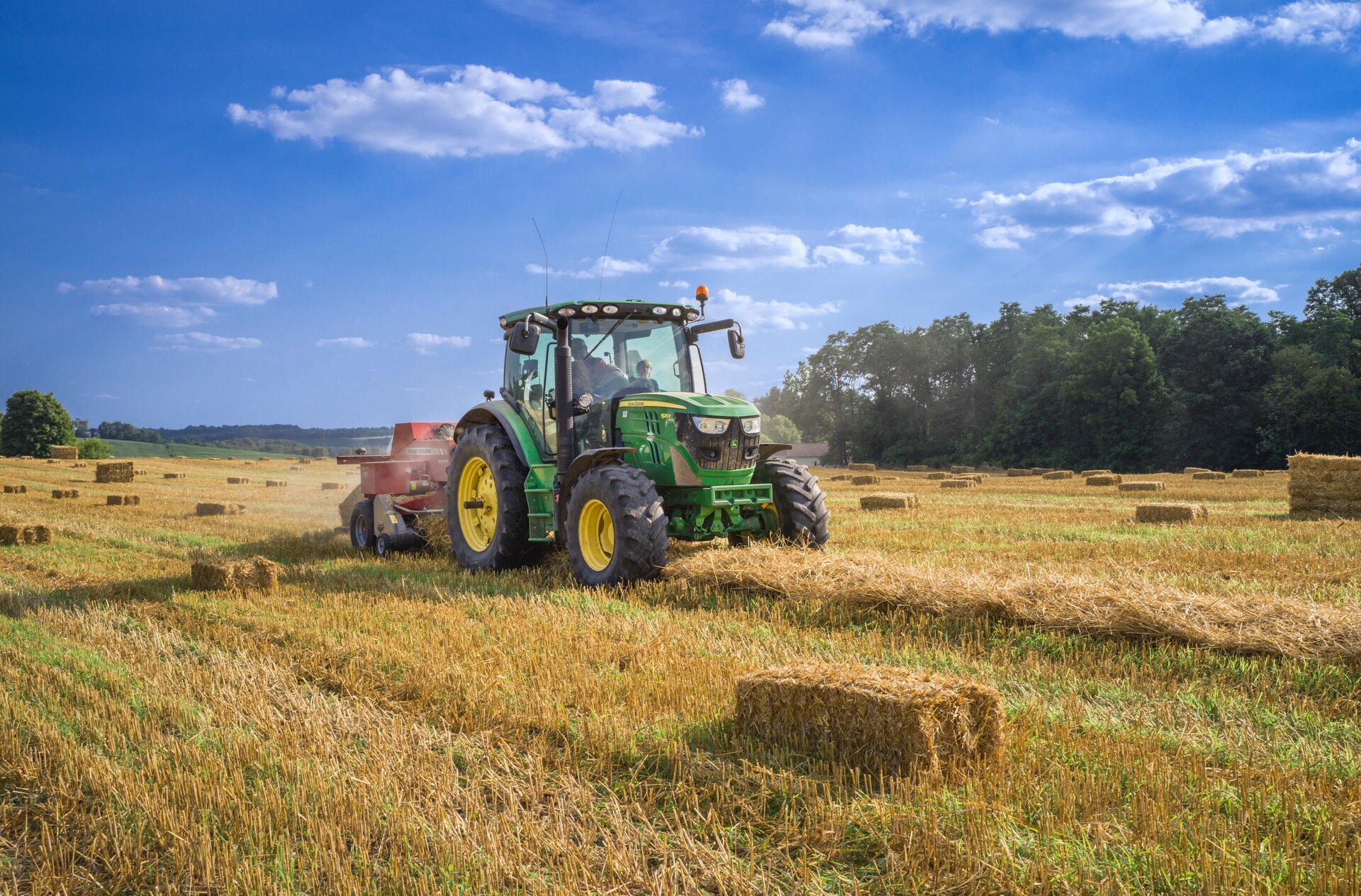 Krok trzeci. Zbiór upraw. Przedstawiony jest traktor z maszyną rolniczą przymocowaną z tyłu. Traktor jedzie po polu, kosząc trawę. Na polu w różnych miejscach znajdują się snopki siana.