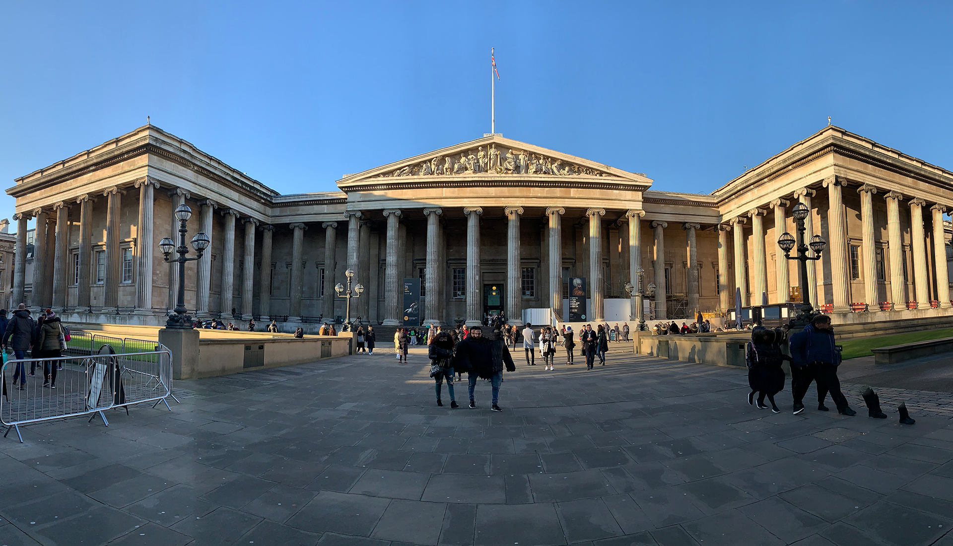  Zdjęcie przedstawia budynek muzeum brytyjskiego oraz plac znajdujący się przed nim. Budynek ozdobiony jest czterdziestoma czterema kolumnami w stylu jońskim oraz trójkątnym tympanonem z płaskorzeźbami. Na placu przed muzeum znajduje się wielu turystów.