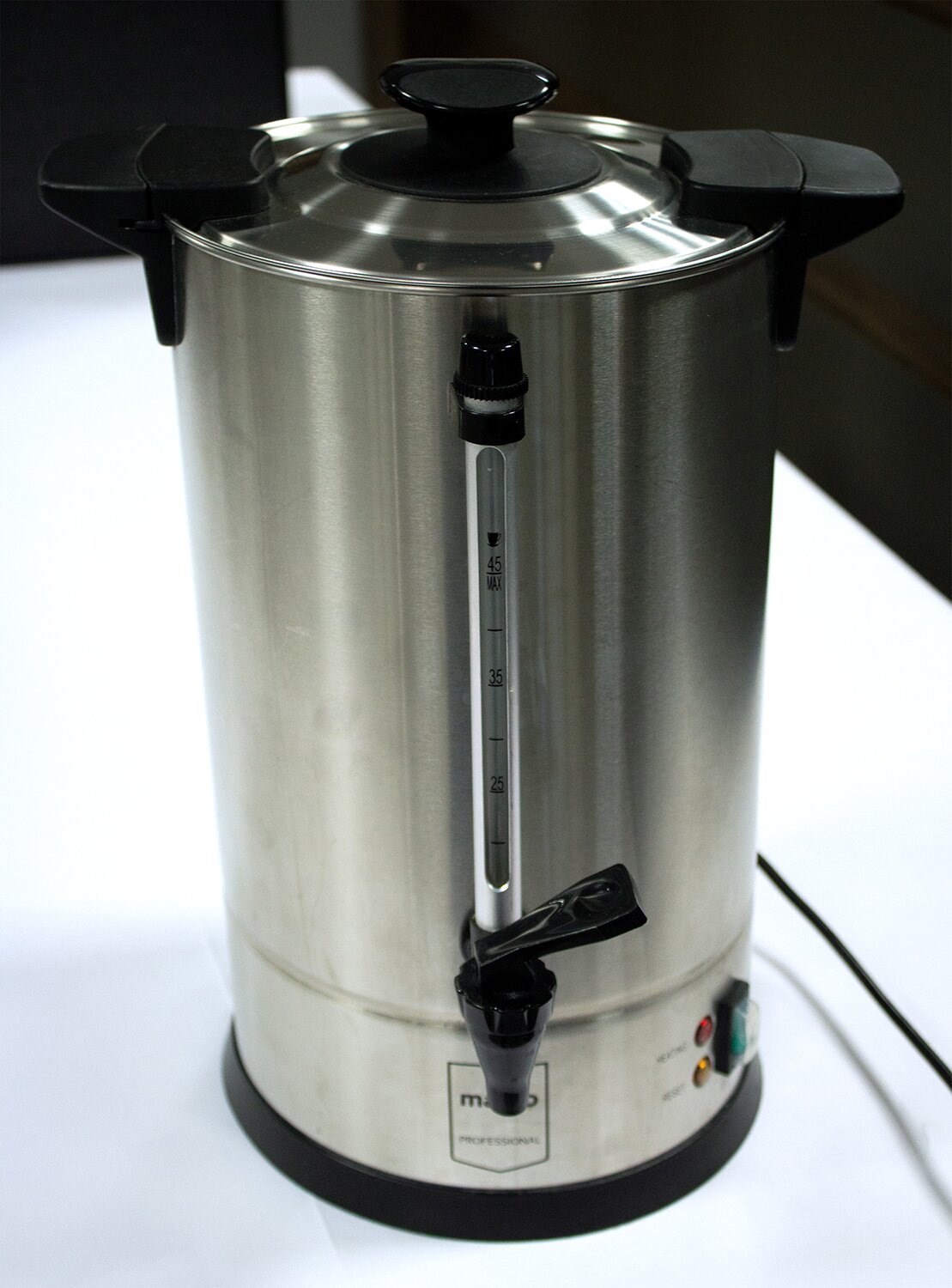 Na zdjęciu znajduje się wysoki  srebrny termos do cateringowego transportu napojów. Wystaje z niego czarny kranik.