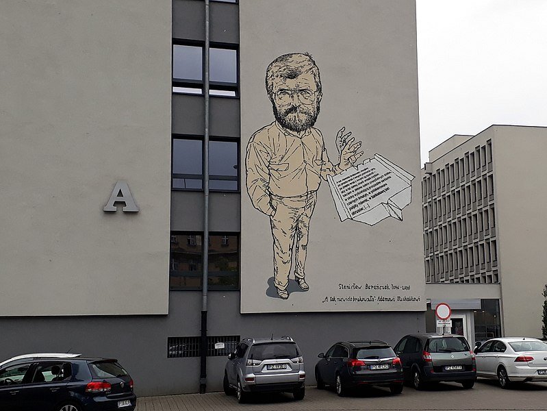 Mural przedstawiający podobiznę postaci Stanisława Barańczaka. Na ścianie dużego budynku znajduje się mural prezentujący dojrzałego mężczyznę w koszuli, spodniach. Mężczyzna ma owalną twarz, zarost, nosi okulary. Puszcza lewą dłonią papierowy samolocik zrobiony z zapisanej kartki.