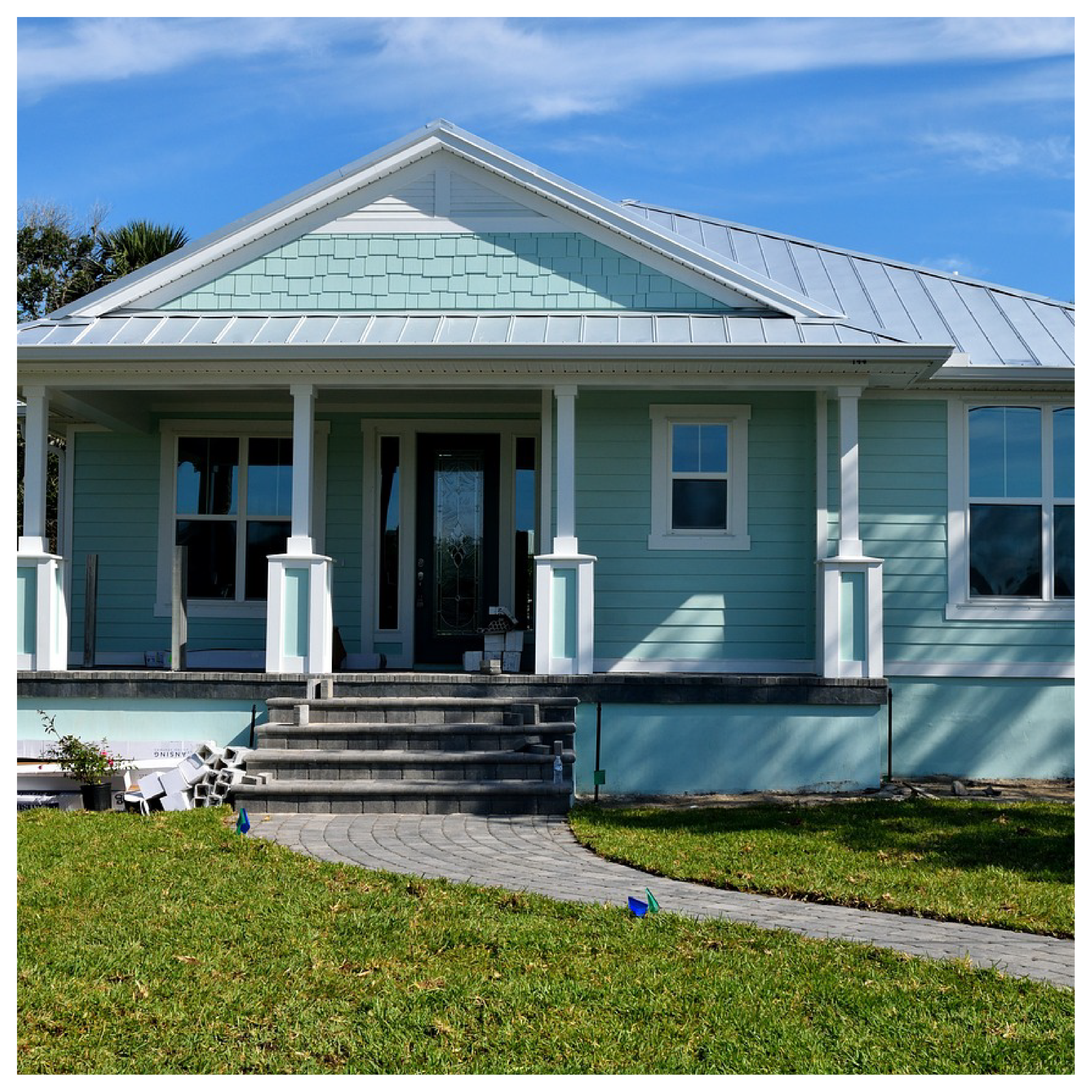 Zdjęcie przedstawia mały, niebieski dom jednorodzinny z ogrodem. 