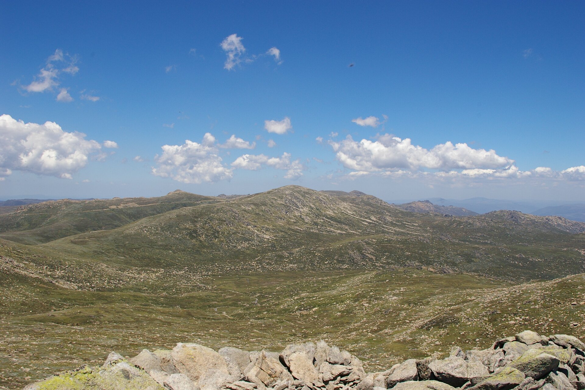 Fotografia prezentuje panorama łagodnych łańcuchów górskich pokrytych trawą i kamieniami. Najwyższe wzniesienie, to Góra Kościuszki.
