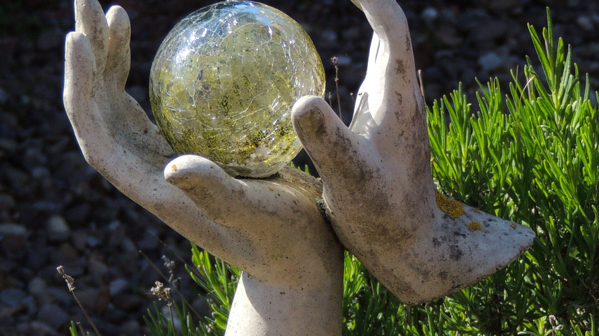 Zdjęcie przedstawia rzeźbę. Ukazane są dwie ludzkie dłonie. Trzymają one szklaną kulę. 