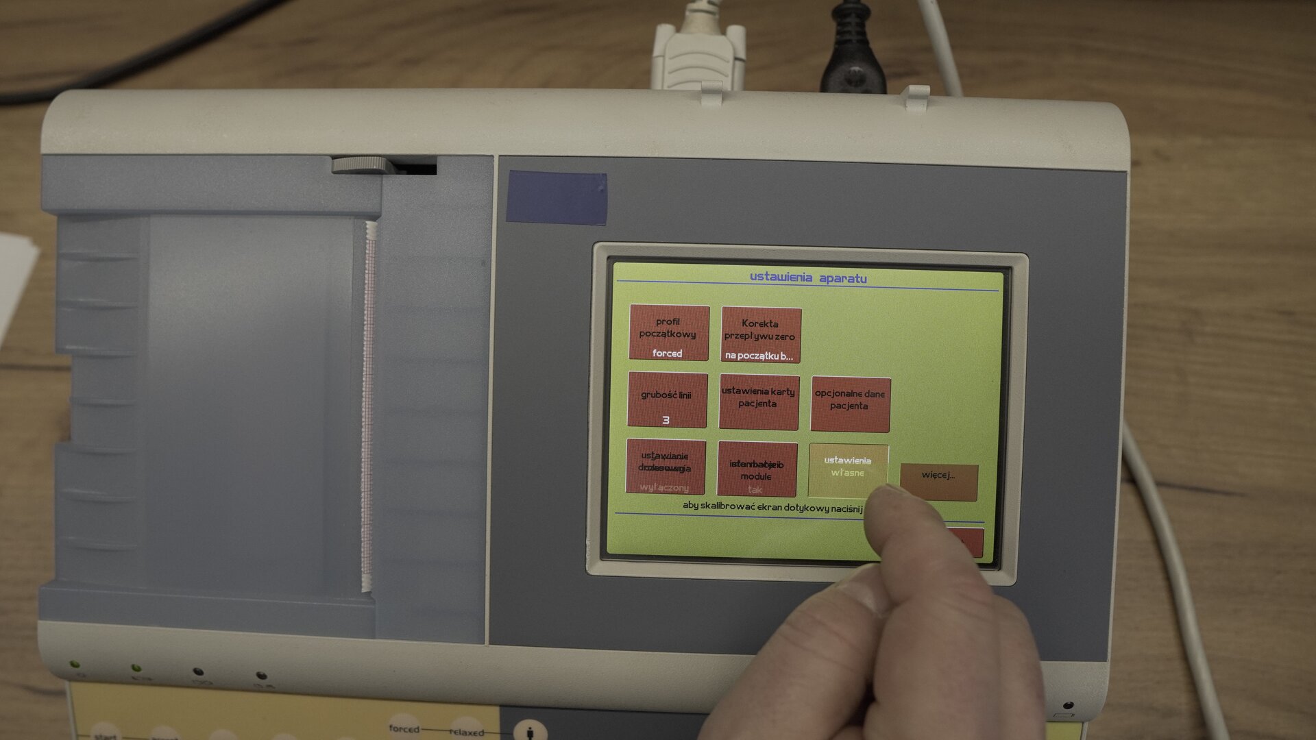 Na zdjęciu technik wybiera na klawiaturze ekranowej spirometru przycisk Ustawienia własne.