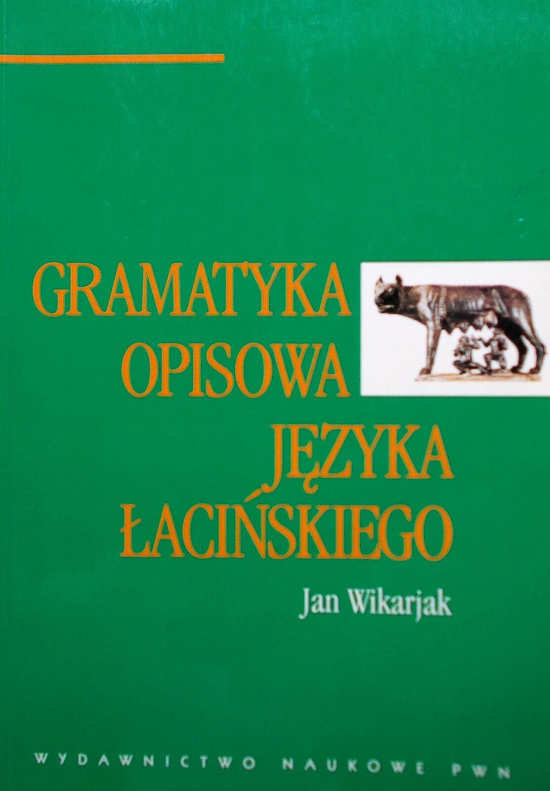 Fotografia nieznanego autora przedstawia widok na stronę tytułową Gramatyki opisowej języka łacińskiego autorstwa Jana Wikarjaka. Okładka książki jest zielona i posiada gładką fakturę, na środku widnieje tytuł książki oraz autor, z prawej strony, obok napisu znajduje się ilustracja przedstawiająca słynną wilczycę, która karmi Remusa i Romulusa – legendarnych założycieli Rzymu. 