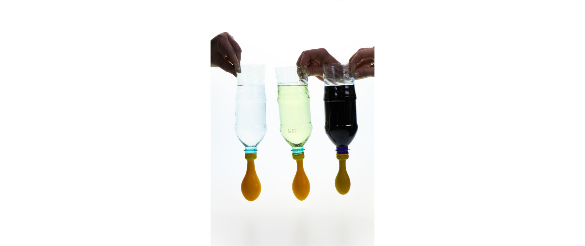 Ilustracja przedstawia trzy przezroczyste butelki plastikowe, które mają odcięte dna i trzymane są do góry nogami. Na każdą z butelek zamiast zakrętki założony jest balonik i uszczelniony gumką recepturką. W każdej z nich znajduje się taka sama objętość różnych cieczy, od lewej – woda, denaturat, olej. Widać różnicę w wielkości baloników; ostatni trzeci napełniony olejem jest najmniejszy.