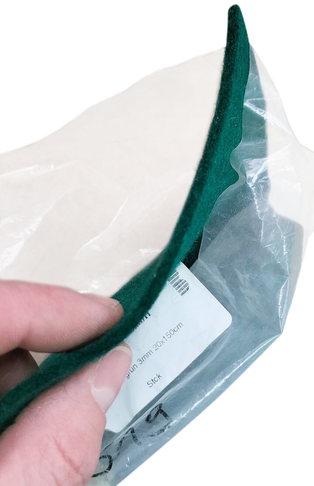 Zdjęcie przedstawia filc bity stosowany do mechanizmach fortepianowych na listwę oporową młotków. Widoczny jest płat filcu bitego w kolorze zielonym, w ujęciu z boku, w przeźroczystym foliowym opakowaniu z białą etykietą z czarnymi napisami.