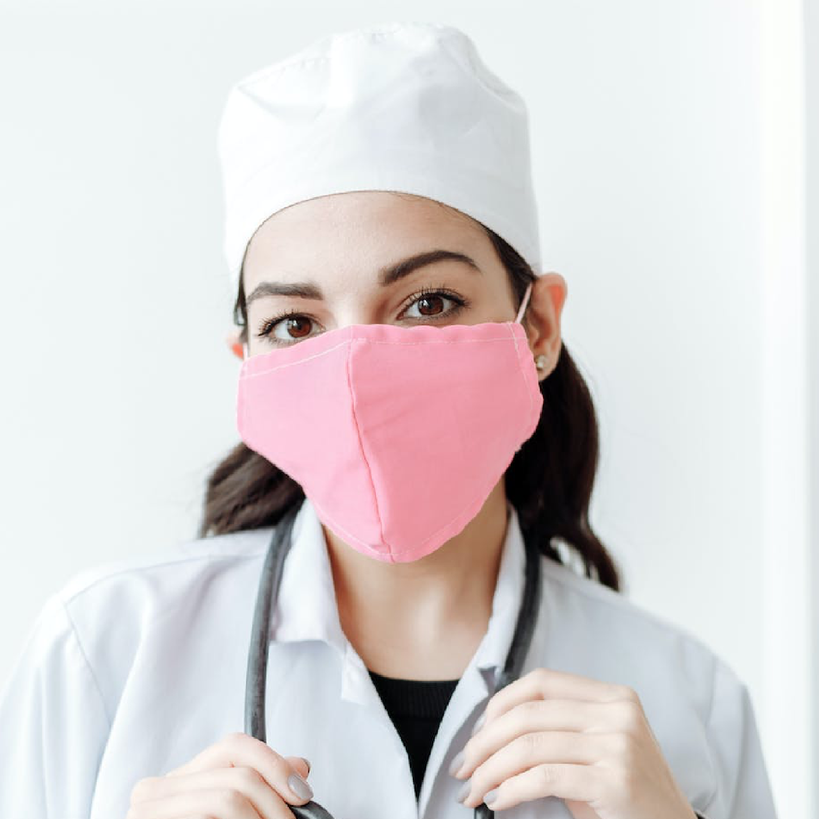 Zdjęcie przedstawia kobietę ubraną w biały fartuch, która na szyi ma przewieszony stetoskop. Na głowie ma biały czepek a na twarzy maskę. 