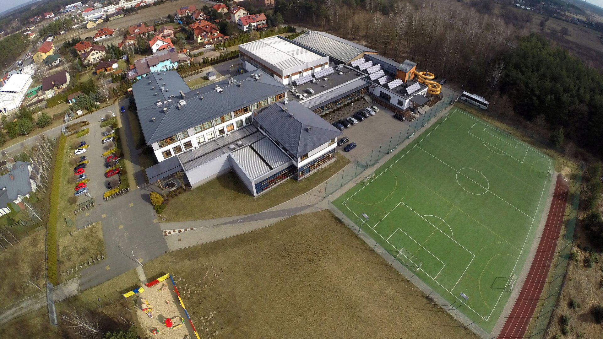 Zdjęcie przedstawia widok z góry na budynek. Obok niego jest boisko piłkarskie. 