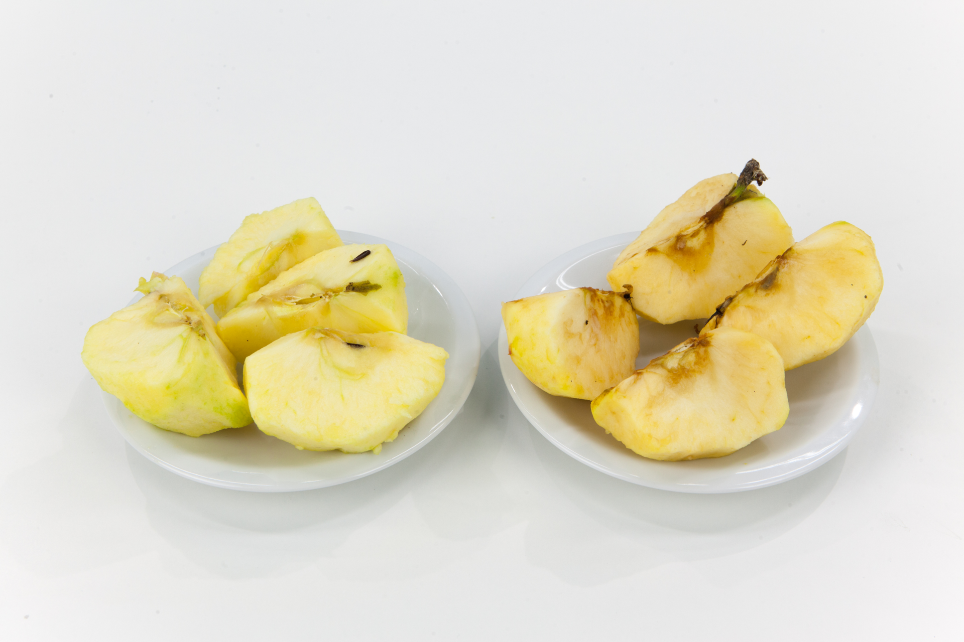 Zdjęcie przedstawia dwa talerzyki, na których znajdują się obrane i pocięte na ćwiartki jabłka. Na talerzyku po prawej stronie miąższ jabłka uległ naturalnemu ciemnieniu.