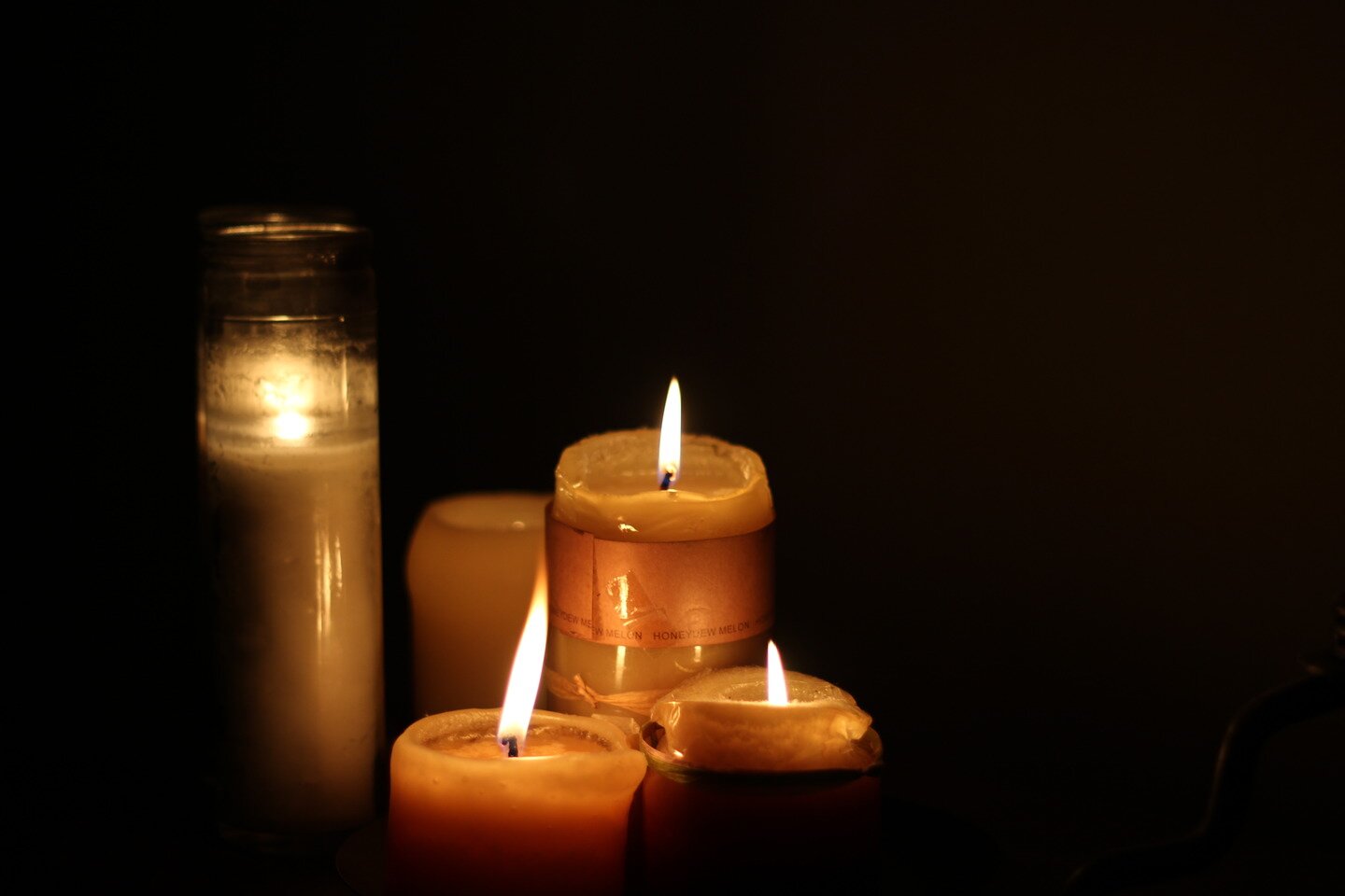 Fotografia przedstawia pięć palących się grubych świec woskowych na czarnym tle.
