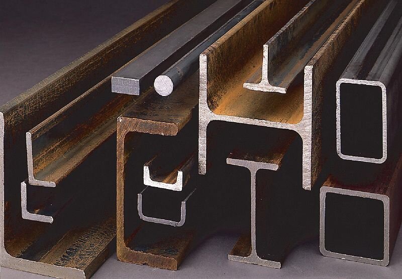 Zdjęcie przedstawia różne rodzaje kształtowników. Znajdują się tam kątowniki (przekrój w kształcie litery „L”), ceowniki (przekrój w kształcie litery „C”), dwuteowniki (przekrój w kształcie litery „H”), teowniki (przekrój w kształcie litery „T”), profile o przekroju kwadratowym, profile o przekroju prostokątnym, a także pręty o przekroju prostokątnym i okrągłym. 