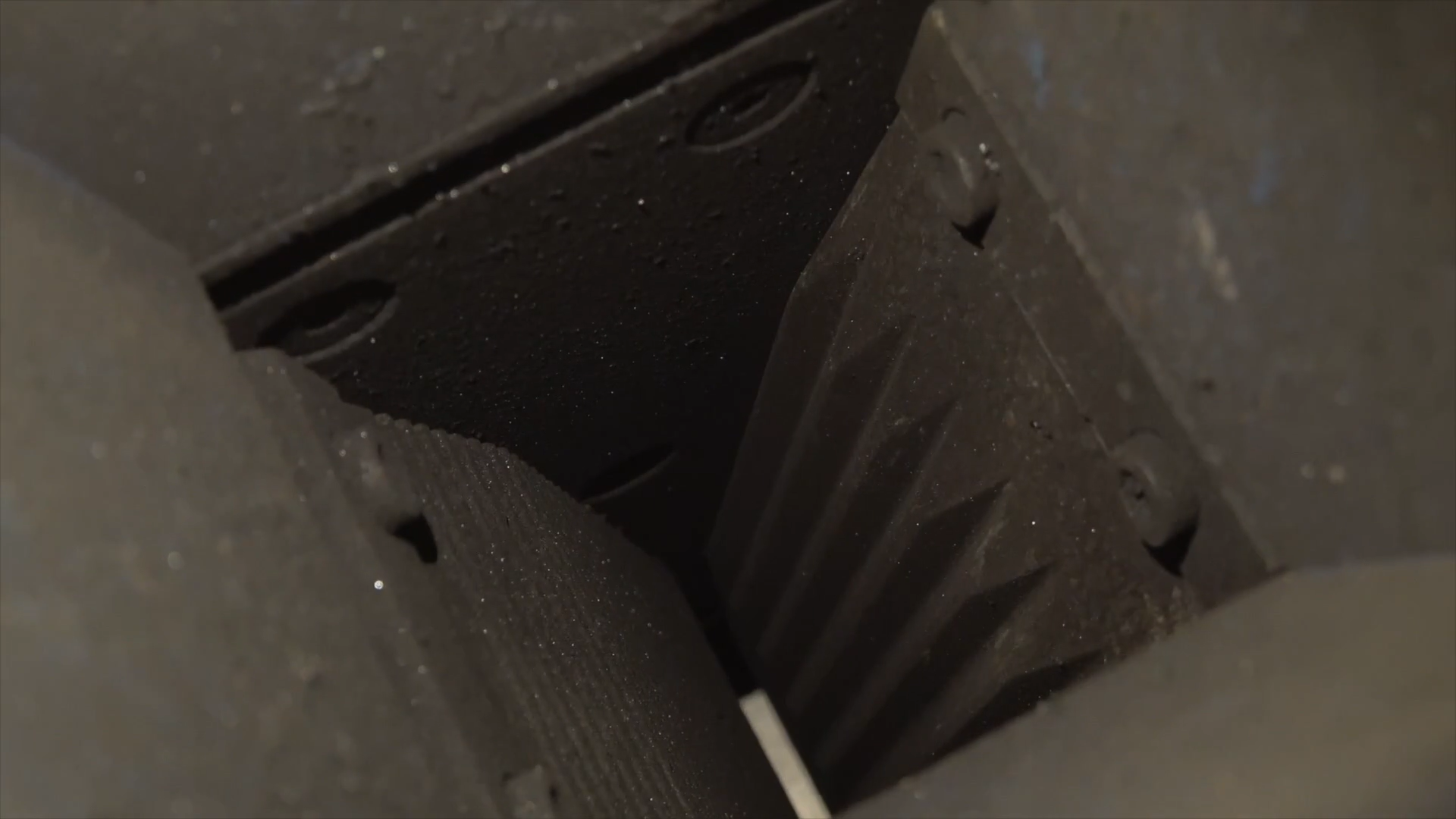 Zdjęcie przedstawia wlot kruszarki szczękowej. We wnętrzu znajdują się dwie szczęki. Stanowią je skierowane do siebie rowkowaną powierzchnia płyty. Rowki poprowadzone są od góry do dołu. Szczęki tworzą kąt ostry, zbliżając się do siebie dolną krawędzią.