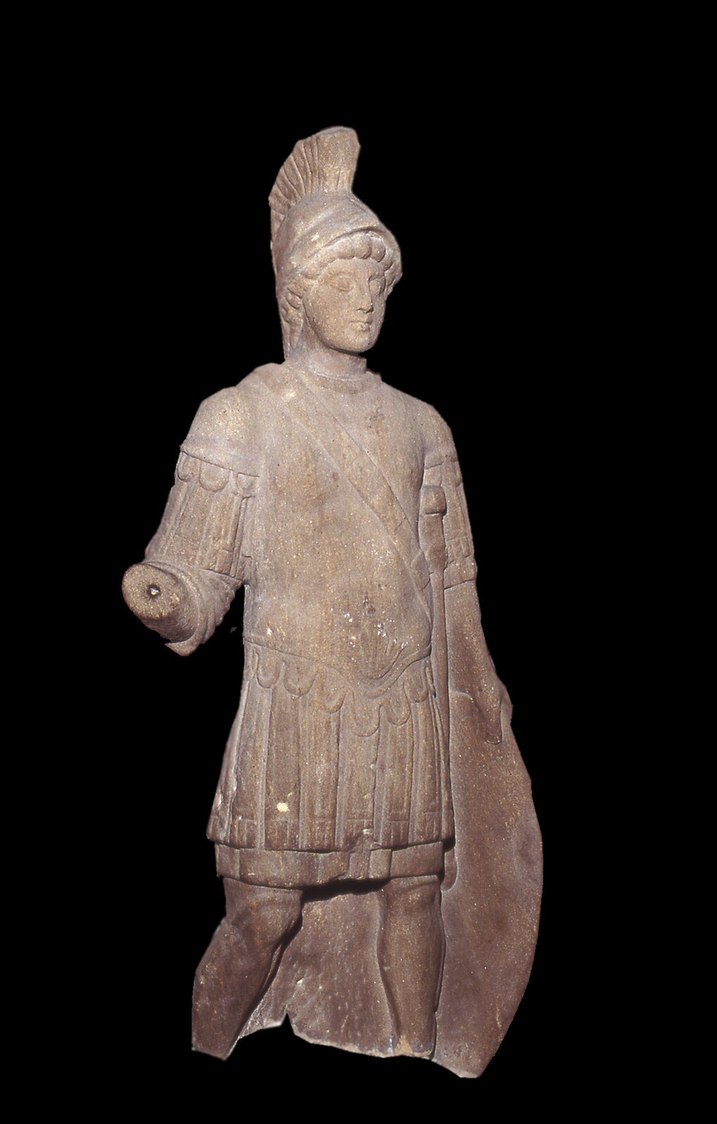 Zdjęcie przedstawia statuę stojącego mężczyzny wykonaną z jasnego kamienia. Ubrany jest w lekką zbroję. W lewej ręce trzyma tarczę, zaś prawa ręka rzeźby została utrącona.