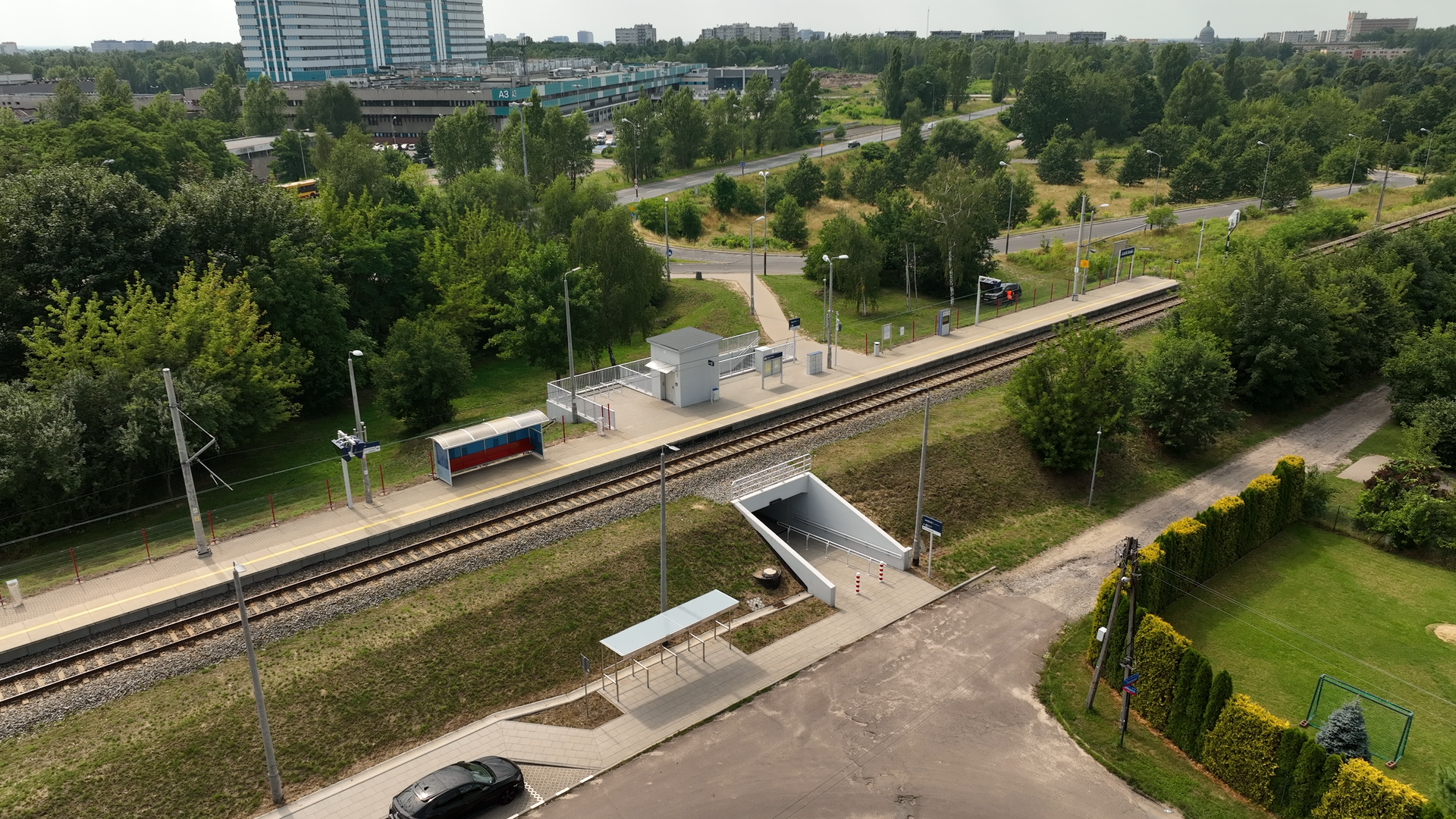 Ilustracja przedstawia przejście pod torami, widoczne z góry. Widoczny jest nasyp kolejowy z pojedynczym torem z niewielkim peronem. Na górze widoczne są schody w dół do przejścia pod torami. Po drugiej stronie nasypu widoczne jest wyjście z przejścia.