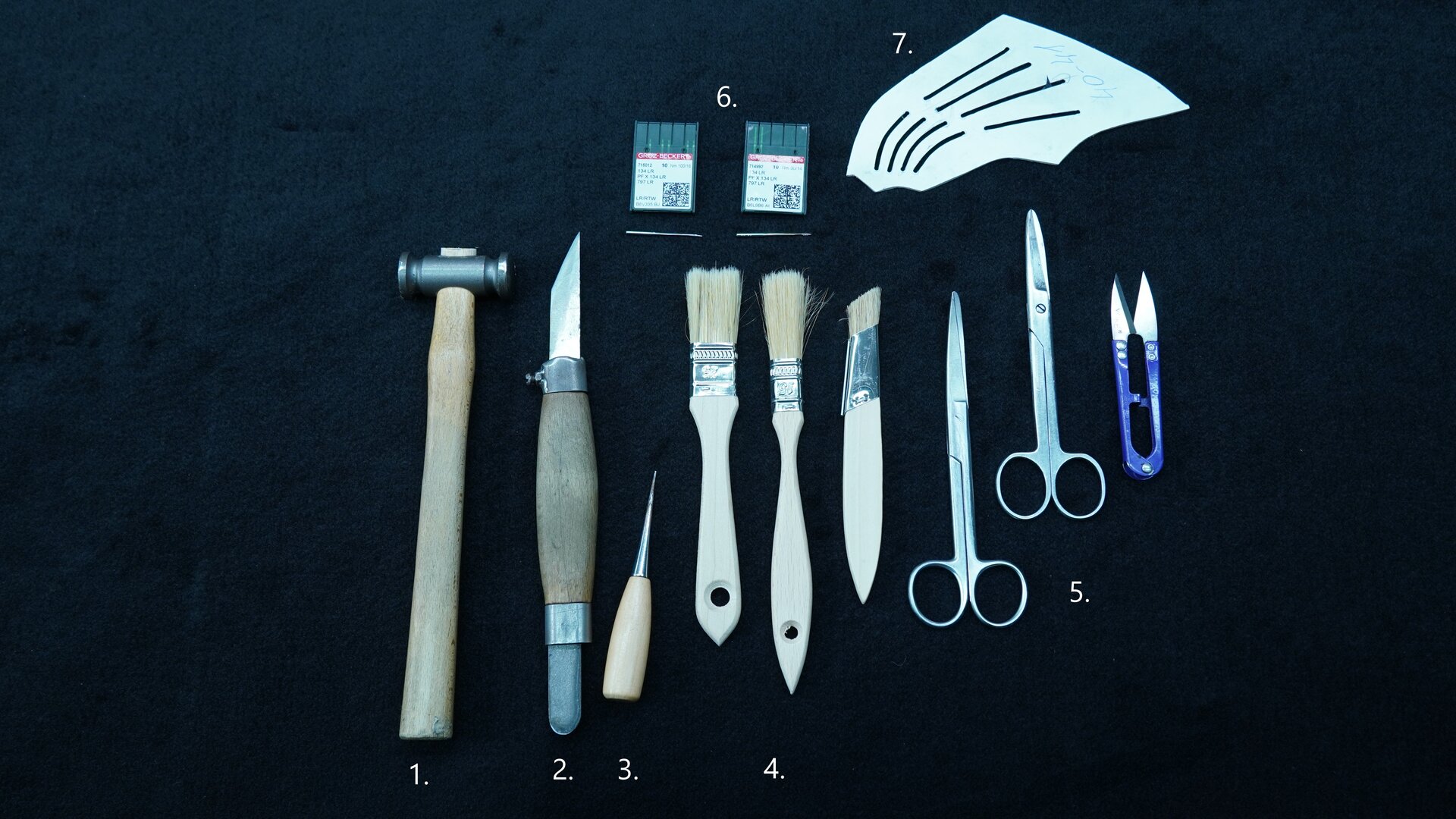Zdjęcie przedstawia leżące koło siebie narzędzia: na górze są dwa małe, płaskie, półprzezroczyste pudełka, pod nimi młotek, nóż, ostrze, małe pędzelki, dwie pary nożyczek, urządzenie przypominające małe szczypce. Nagranie tożsame z treścią.