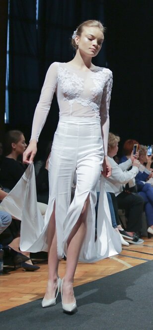 Zdjęcie przedstawia modelkę prezentującą białą, obcisłą sukienkę z koronkowym topem i rozciętą spódnicą.